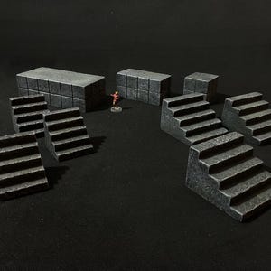 Op de afbeelding: Een verzameling grijze, steen-getextureerde miniatuur terreinstukken voor tabletop gaming. De set bevat verschillende trappen, rechthoekige blokken en een klein figuur, allemaal gerangschikt op een donkere ondergrond. Ideaal voor een kerker- of kasteelsetting.