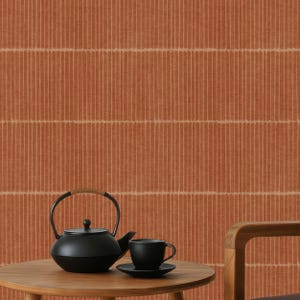 May include: A black teapot with a wooden handle sits on a round wooden table, next to a black teacup and saucer. The background features a textured, vertical-striped orange wall.