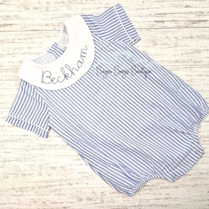 May include: Blue and white striped baby romper with a white collar. The collar has the name "Beckham" embroidered in black script. The romper has short sleeves and snap closures.