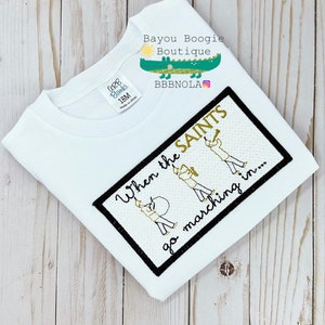 Peut inclure: T-shirt blanc &agrave; manches courtes avec un motif rectangulaire bord&eacute; de noir. Le motif pr&eacute;sente le texte "When the SAINTS go marching in..." et des illustrations de membres d'un groupe de musique. Le t-shirt porte une &eacute;tiquette "CORB Blanks 18M Made in china".