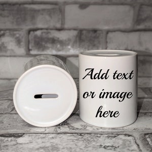 May include: Two white ceramic money banks. One bank is upright, with the text "Add text or image here" in black script. The other bank is on its side, showing a slot for inserting money. The banks are cylindrical.