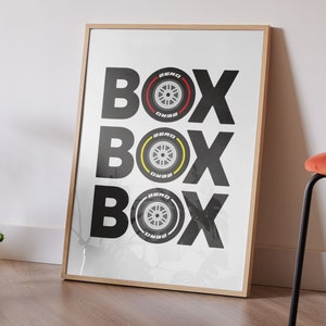 May include: A framed print with the word "BOX" repeated three times in black text. Each "BOX" has a black and white tire with red and yellow accents in the center.