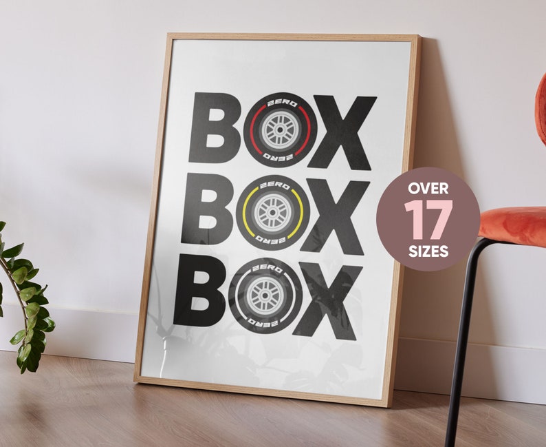 May include: A white poster with the word "BOX" repeated three times in black. Each "BOX" has a black and yellow tire graphic inside. The poster is framed in a light wood frame. The text "OVER 17 SIZES" is in a circle on the right side of the poster.