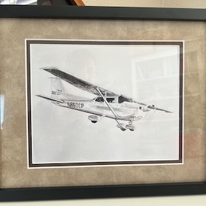Puede incluir: Un dibujo a lápiz en blanco y negro de un avión pequeño en un marco marrón. El avión es un Cessna 172 con el número de cola N850CP.