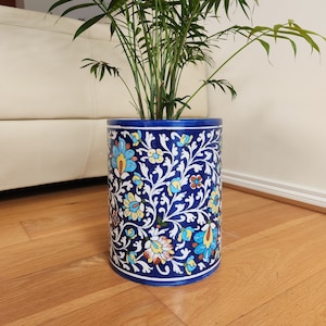 May include: A blue ceramic planter with a floral pattern in shades of yellow, blue, and white. The planter is filled with a green plant.