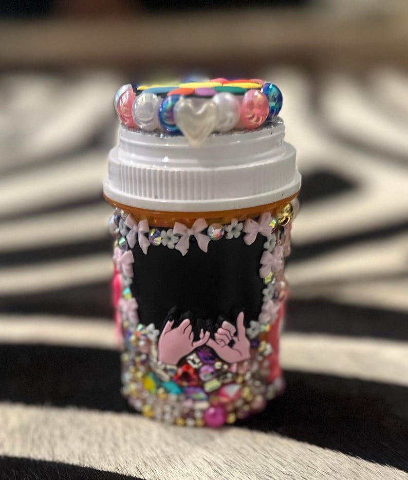 Bedazzled pill bottle with colorful beads, rhinestones, pearls, and a pink octopus charm, with a chalkboard label