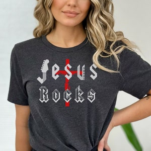 May include: A dark gray t-shirt with a white graphic design that says "Jesus Rocks" with a red cross and a guitar.