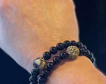 May include: A black beaded bracelet with two accent beads. One bead is black and white, and the other is brown and white.