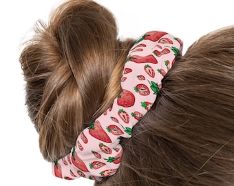 May include: A pink scrunchie with a strawberry print. The scrunchie is tied around a woman's hair in a bun.
