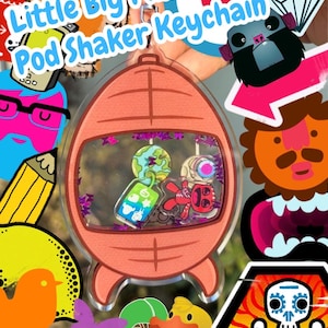 May include: A clear, pod-shaped keychain with the text "Little Big Planet Pod Shaker Keychain." The keychain has a peach-colored frame with a clear center, showcasing miniature planet and character charms. The design includes a variety of colorful cartoon graphics.