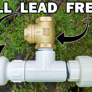 May include: A plumbing assembly featuring a brass valve and white PVC pipes, with the text "ALL LEAD FREE" in a bold, white font. The assembly includes a red valve handle and is set against a backdrop of green foliage.