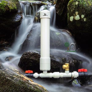 May include: A white PVC pipe water filtration system with red and brass valves is set against a natural waterfall backdrop. The system is designed to filter water, with a vertical pipe and horizontal components.