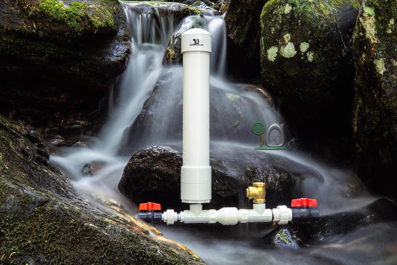 May include: A white PVC pipe water filtration system with red and brass valves is set against a natural waterfall backdrop. The system is designed to filter water, with a vertical pipe and horizontal components.