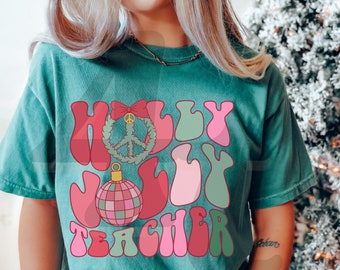 May include: Teal-colored t-shirt with the words "Holly Jolly Teacher" in a retro font. The design includes a peace sign, a Christmas ornament, and a bow. The shirt is a comfortable, casual style.
