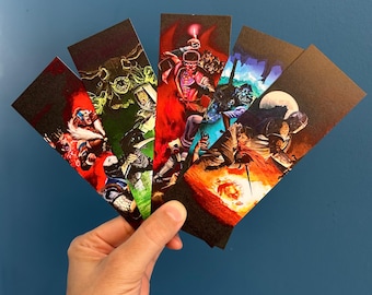 May include: A hand holds a fanned stack of five rectangular bookmarks. Each bookmark features a vibrant, detailed illustration with a dark background. The illustrations depict various characters in action, with a mix of colors including red, green, and blue.