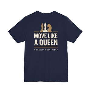 May include: A navy blue short-sleeve t-shirt featuring a graphic print in cream and tan. The design includes three chess pieces above the text "MOVE LIKE A QUEEN" and the words "BRAZILIAN JIU-JITSU" printed in a clean, sans-serif font below.