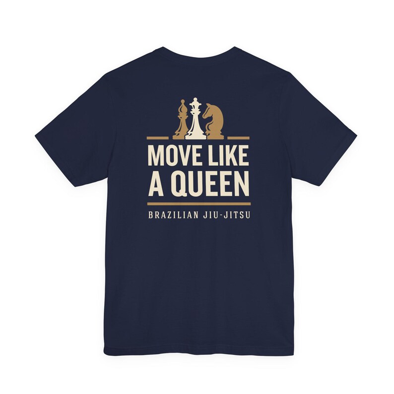 May include: A navy blue short-sleeve t-shirt featuring a graphic print in cream and tan. The design includes three chess pieces above the text "MOVE LIKE A QUEEN" and the words "BRAZILIAN JIU-JITSU" printed in a clean, sans-serif font below.
