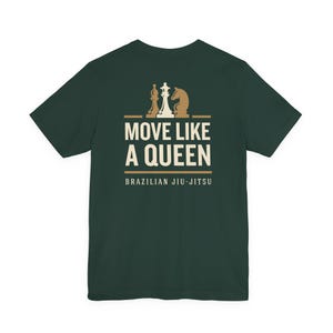 May include: A dark green short-sleeve t-shirt featuring a graphic on the back. The design includes three chess pieces above the text MOVE LIKE A QUEEN and the words BRAZILIAN JIU-JITSU in a light cream color, centered on the upper back area.