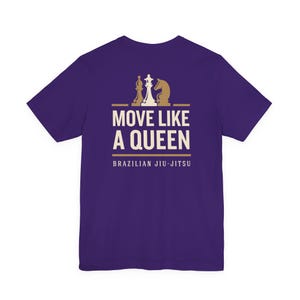 May include: A purple short-sleeve t-shirt featuring a graphic print in cream and gold. The design includes three chess pieces above the text MOVE LIKE A QUEEN and the words BRAZILIAN JIU-JITSU printed in a clean, sans-serif font below.