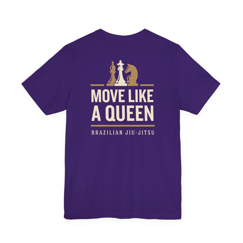 May include: A purple short-sleeve t-shirt featuring a graphic print in cream and gold. The design includes three chess pieces above the text MOVE LIKE A QUEEN and the words BRAZILIAN JIU-JITSU printed in a clean, sans-serif font below.