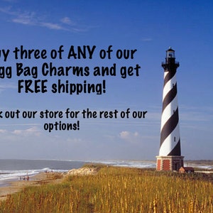 May include: A black and white striped lighthouse stands tall on a grassy dune overlooking a sandy beach and ocean. The text "Buy three of ANY of our Bogg Bag Charms and get FREE shipping! Check out our store for the rest of our options!" is displayed in the upper left corner of the image.