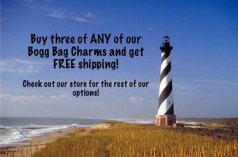 May include: A black and white striped lighthouse stands tall on a grassy dune overlooking a sandy beach and ocean. The text "Buy three of ANY of our Bogg Bag Charms and get FREE shipping! Check out our store for the rest of our options!" is displayed in the upper left corner of the image.