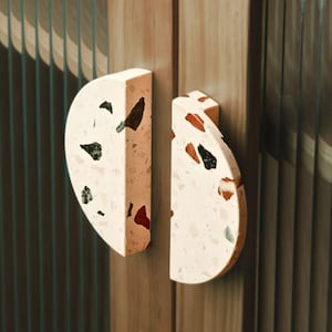 May include: Two half-circle cabinet pulls made of terrazzo with a white base and flecks of red, black, and green.