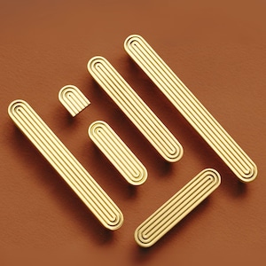 May include: A set of six gold-toned metal cabinet pulls with a grooved design. The pulls are arranged in a staggered pattern on a brown background.
