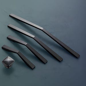 May include: Five black metal cabinet pulls in different sizes, with a square knob in the centre. The pulls have a modern, minimalist design.