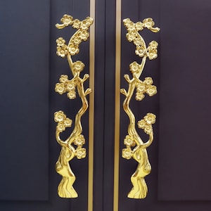 May include: A pair of gold door handles with a floral design. The handles are shaped like branches with leaves and flowers.