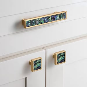 May include: A set of three cabinet hardware pulls with a gold finish and iridescent abalone shell inlay. The set includes one long pull and two square knobs.