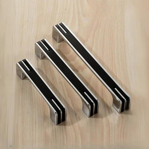 May include: Three black and silver cabinet pulls with a modern design. The pulls are different sizes and have a black insert with silver lines.