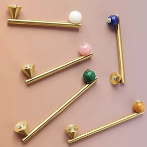 May include: Six gold cabinet knobs with different colored gemstone spheres. Each knob has a diamond-shaped accent on the top.