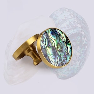 May include: Two round brass cabinet knobs with a green, blue, and purple iridescent abalone shell inlay.