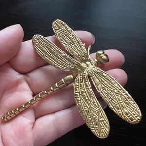 Puede incluir: Una lib&eacute;lula de metal dorado con alas detalladas. La lib&eacute;lula mide aproximadamente 12,5 cm de largo.