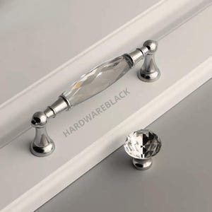 May include: A pair of crystal cabinet knobs with a silver finish. The larger knob is a pull handle with a faceted crystal design. The smaller knob is round with a faceted crystal design.