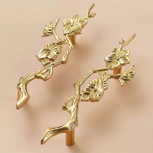 May include: Two gold-toned cabinet pulls shaped like stylized branches with delicate flower details.