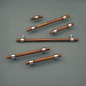 May include: A selection of wooden cabinet handles with silver metal detailing. The handles are various sizes, with the longest measuring about 30 cm in length. The wood is a deep brown, and the metal has a shiny silver finish.