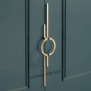 May include: A gold-toned door handle with a circular design and two vertical lines. The handle is mounted on a dark blue door.