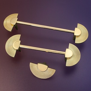 May include: Three gold-toned metal curtain rods with decorative fan-shaped finials. The finials have a sunburst design.