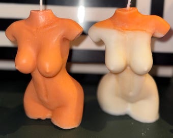 May include: Two torso shaped candles, one is orange and the other is white with an orange top.