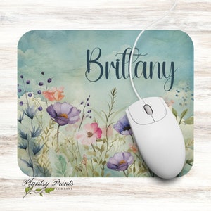 May include: A personalized mousepad with a watercolor floral design in shades of blue, pink, and purple. The name "Brittany" is written in a cursive font at the top of the mousepad.