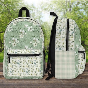 May include: Two backpacks with a floral and leaf pattern. The front backpack has a light green background with white flowers. The bottom section has a leaf pattern. The side backpack has a leaf pattern and a plaid pattern. Both have black zippers and straps.
