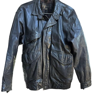 May include: Black leather jacket with multiple pockets, a zip-up front, and a bomber-style design. The jacket has a collared neckline and a ribbed hem. The leather appears worn, giving it a vintage look.