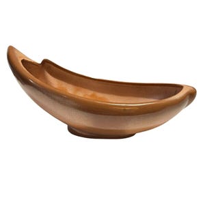 May include: A brown ceramic boat-shaped bowl with a glossy finish. The bowl has a curved design with a wide opening and a slightly raised base. The color is a warm, earthy tone, suitable for decorative or functional use.