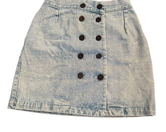 May include: A light blue acid-wash denim skirt featuring a high-waisted design and a double-breasted front closure. The skirt is adorned with ten dark brown circular buttons arranged in two vertical rows, providing a structured look.