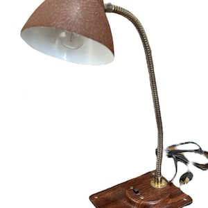 May include: A vintage desk lamp with a brown textured shade and a flexible, silver-toned neck. The lamp has a wooden base with a built-in switch and a power cord. The shade is lined with white. The lamp is designed for desk use.