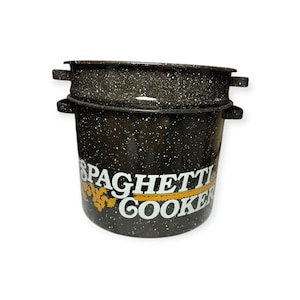 May include: A black enamel spaghetti cooker pot with white speckles and two side handles. The front features white text that reads SPAGHETTI COOKER with a yellow graphic element underneath the word SPAGHETTI. The pot includes a matching insert.