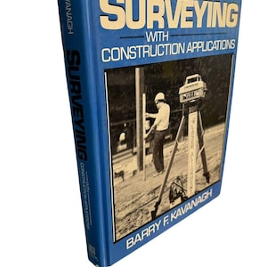 May include: A blue hardcover textbook titled Surveying with Construction Applications by Barry F. Kavanagh. The cover features a black and white photograph of a person using surveying equipment on a tripod at a construction site.