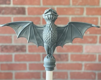 May include: A gray, sculpted bat figurine with outstretched wings, perched atop a round, gray base. The bat has a detailed, textured body and a slightly open mouth.